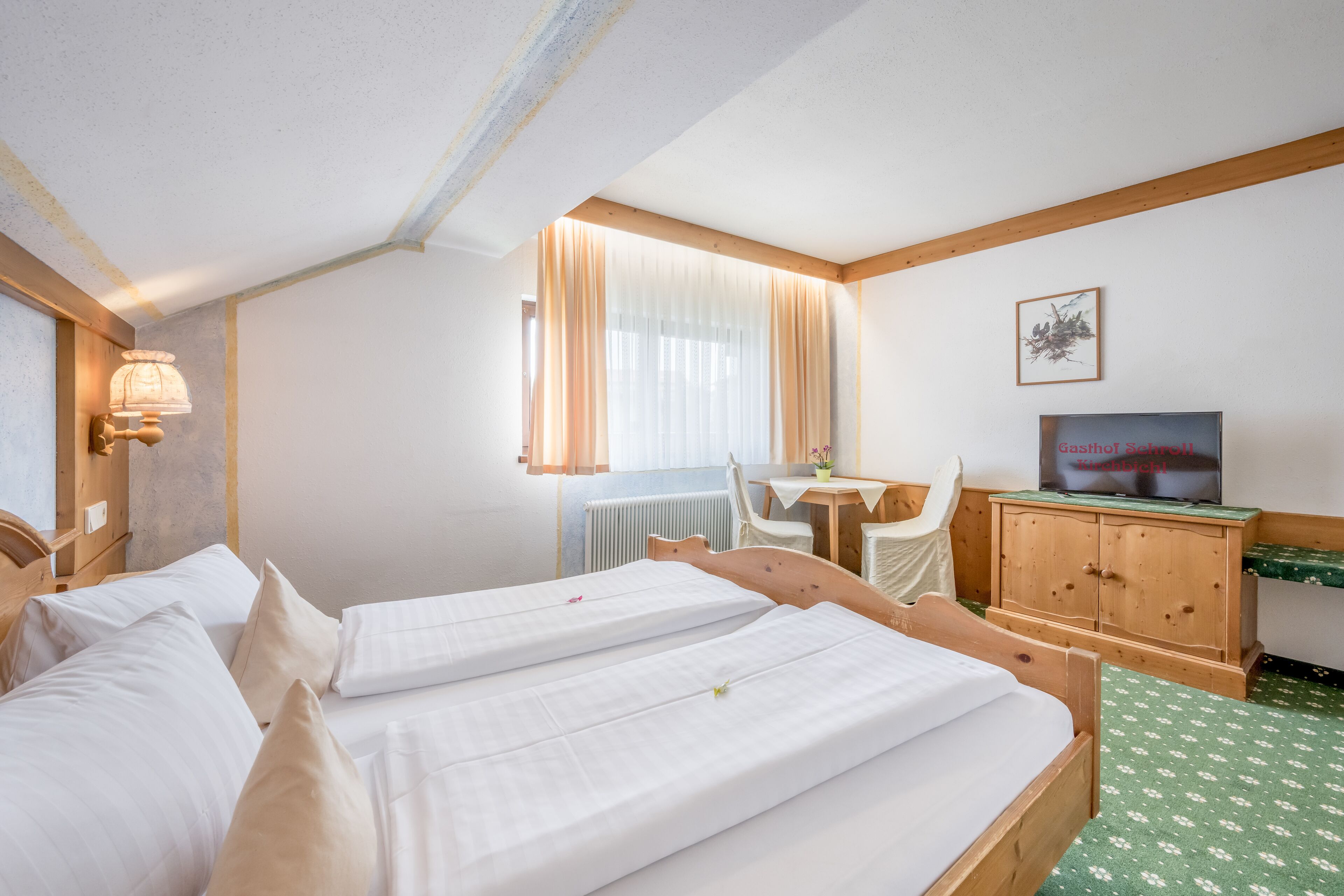 A hotel room with two beds, a wooden desk, a television, and a radiator.
