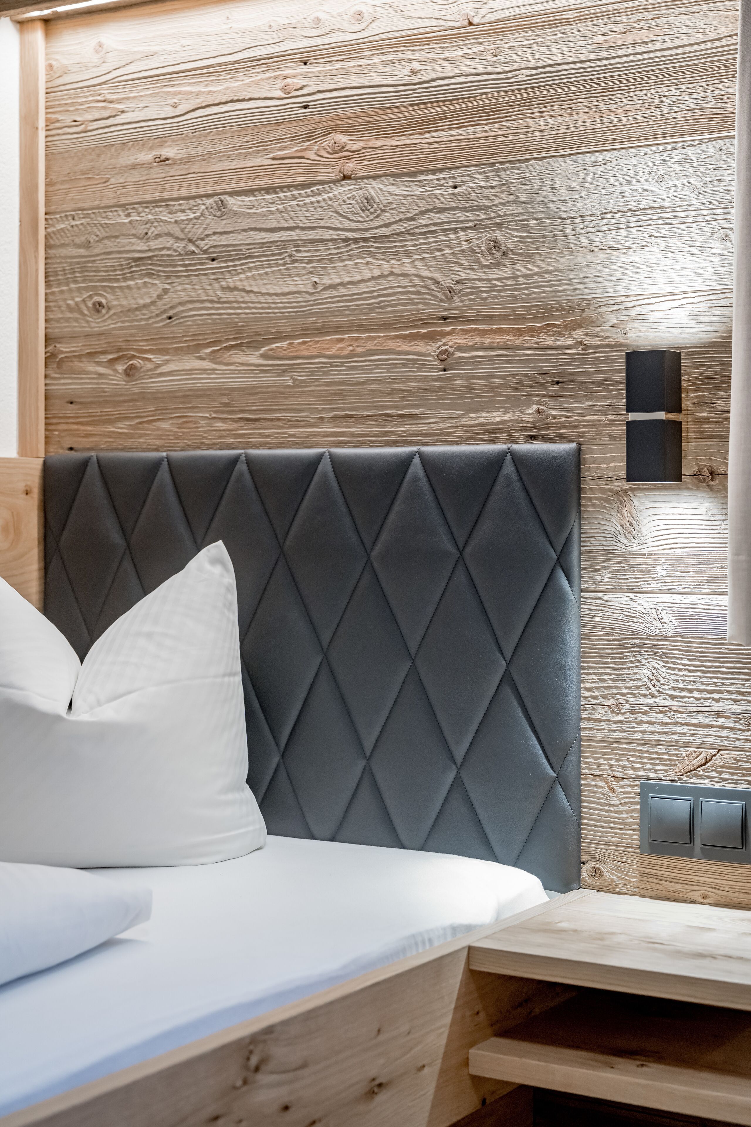 Un lit avec une tête de lit rembourrée de couleur grise, des oreillers blancs et un panneau de tête de lit en bois.