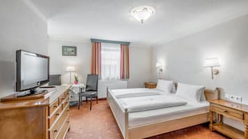 Habitación de hotel con una cama, un escritorio con televisor, una silla, una lámpara y una ventana con cortinas.