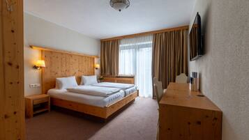 A hotel room with a wooden bed, bedside lamps, a desk, and a flat-screen TV mounted on the wall.