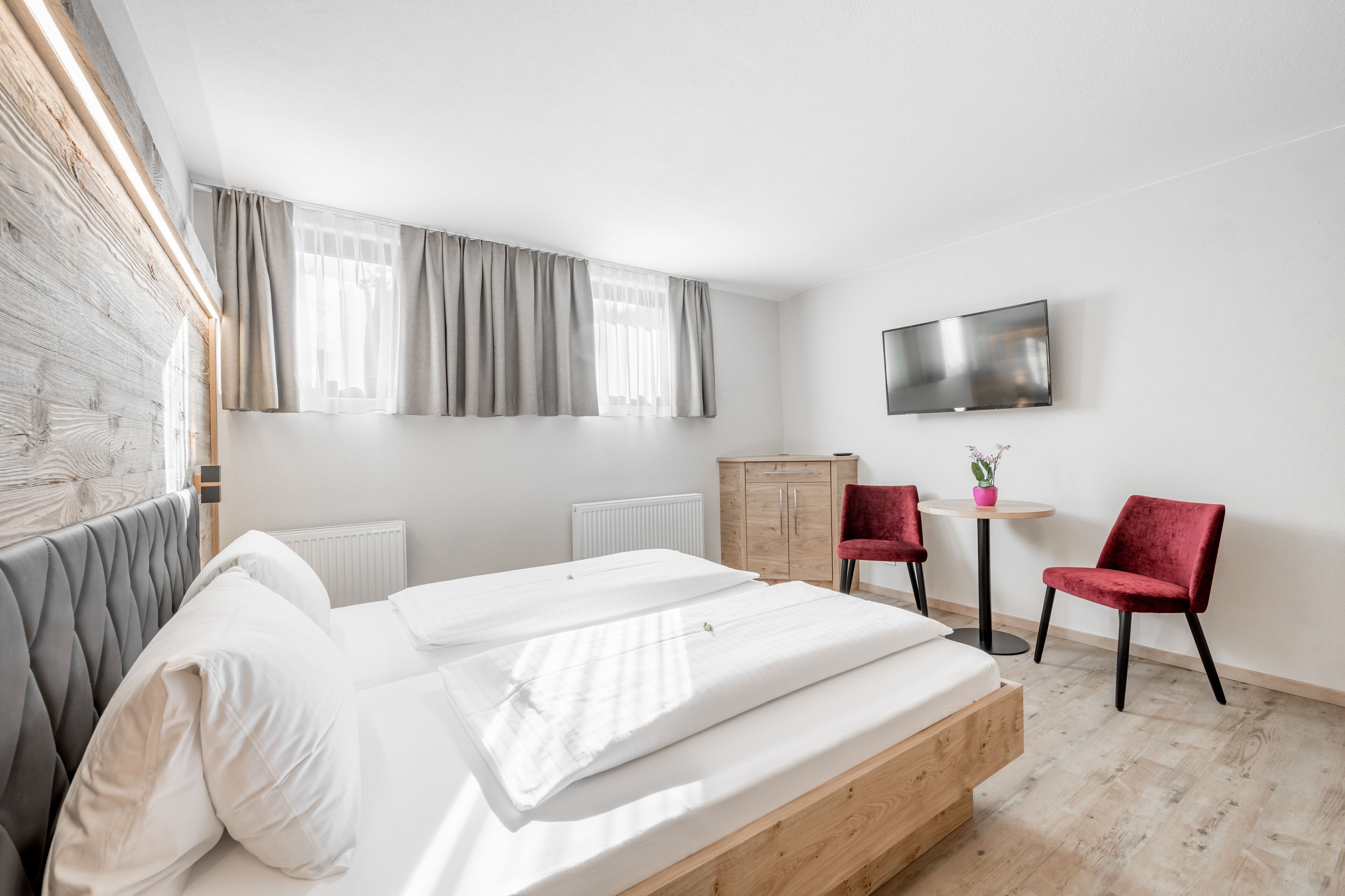 Una habitación de hotel moderna con una cama, un cabecero de madera, un televisor, una mesita con una silla y un radiador.