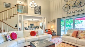 A spacious living room with a white leather sofa, a brown ottoman, and a patterned rug. A staircase with wooden railings leads to an upper level. - Bring Your Pets! Chattanooga Home w/ Dtwn Views (Chattanooga)