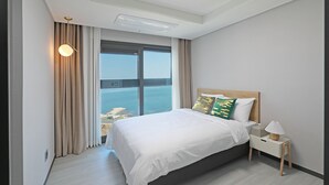 Une chambre d’hôtel moderne avec un grand lit, une table de chevet, une lampe et une vue sur la mer.