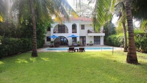 A two-story building with a swimming pool, surrounded by palm trees and a well-maintained lawn.