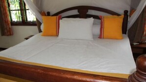 A bed with a wooden headboard, white bedding, and two orange pillows.