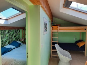 A dormitory room with bunk beds, a skylight, a woven chair, and a framed picture on the wall.