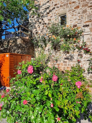 A stone building with a wooden balcony and a garden with pink roses.