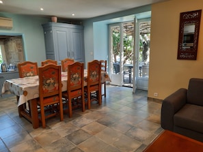 A dining area with a table set for six, wooden chairs with floral upholstery, a blue cabinet, and a sliding glass door leading to an outdoor patio.