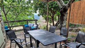 Eine Terrasse im Freien mit Tisch und Stühlen, umgeben von Bäumen und einem Holzzaun.