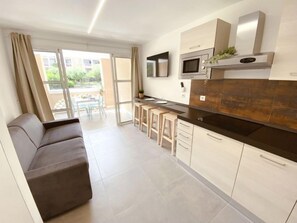 A modern kitchen with a black countertop, white cabinets, and a built-in microwave. There is a sliding glass door leading to an outdoor area with a table and chairs.