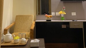 Una sala de estar moderna con un sofá, una mesa de centro con juego de té, un televisor de pantalla plana montado en la pared y un pequeño jarrón decorativo con flores.