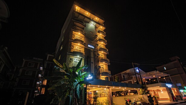 Un hotel de varios pisos con balcones, una entrada bien iluminada y plantas en macetas.
