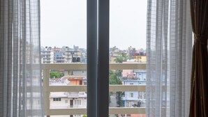Vista a través de una ventana con cortinas traslúcidas, mostrando un área residencial de varios pisos con diferentes edificios y balcones.