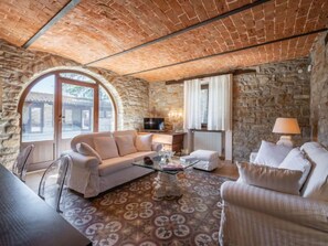 A cozy living room with a stone wall, a white sofa, a glass coffee table, and a lamp.