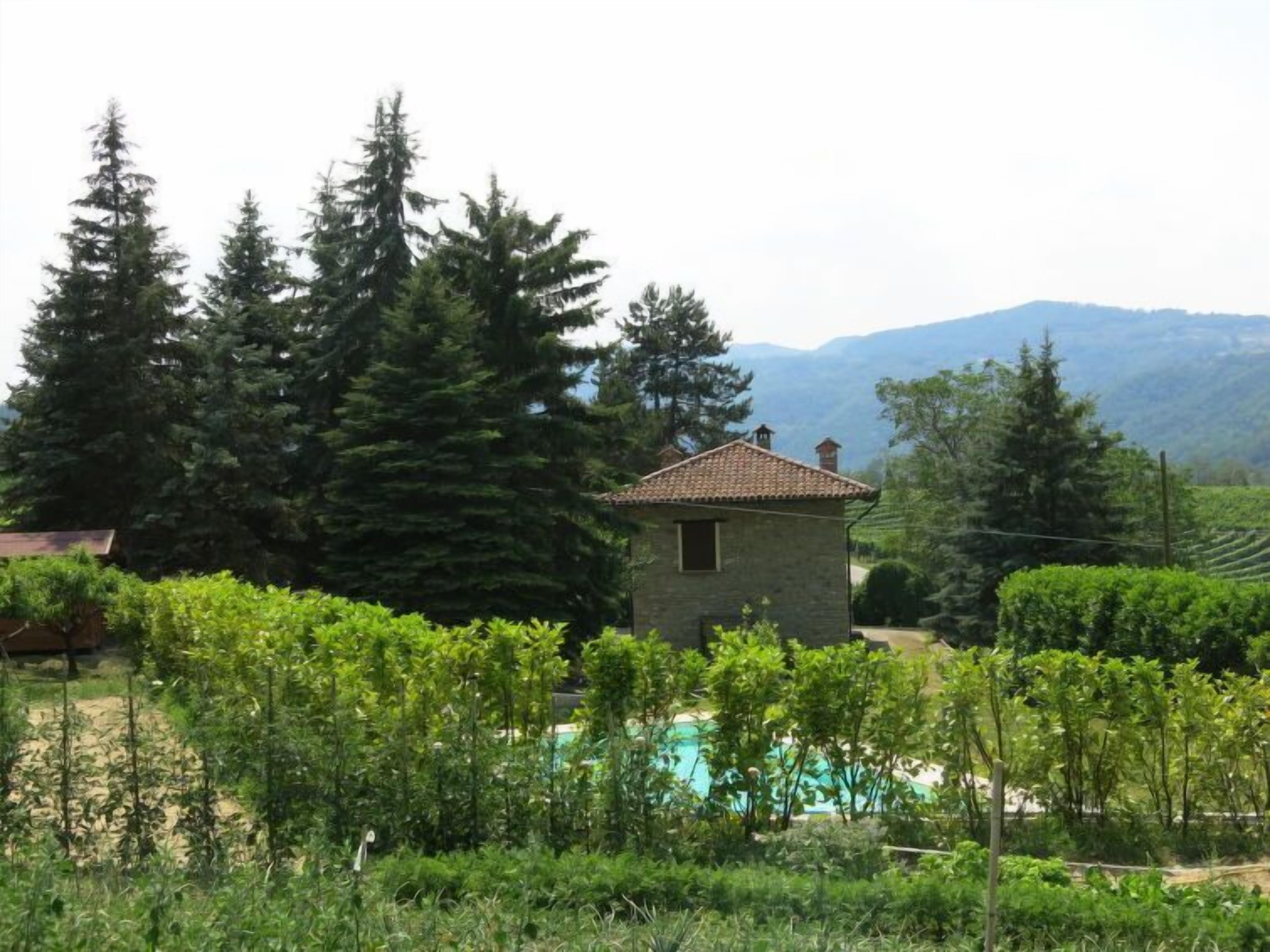Une maison en pierre, avec un toit de tuiles, entourée d’une végétation luxuriante et dotée d’une piscine.