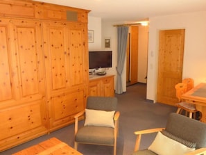 Ein Zimmer mit Holzschrank, Fernseher, grauem Sofa und Esstisch aus Holz.