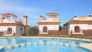 En swimmingpool med en klar blå vandoverflade, omgivet af bygninger med en gennemgående arkitektonisk stil, der inkluderer terracotta-tag og hvide vægge.