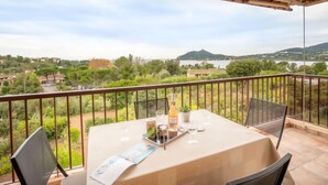 Een balkon met een tafel gedekt voor twee, met uitzicht op een schilderachtig landschap met heuvels en een waterpartij.