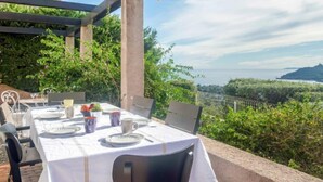 An outdoor dining area with a table set for two, overlooking a scenic view of the sea and greenery. - Maison La Galine by Interhome (Agay Saint Raphael)