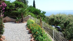 A gravel pathway leading to a coastal area with a view of the sea, surrounded by greenery and a fence. - Maison La Galine by Interhome (Agay Saint Raphael)