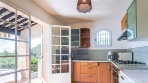 A kitchen with wooden cabinets, a white stove, and a window overlooking greenery. - Maison La Galine by Interhome (Agay Saint Raphael)