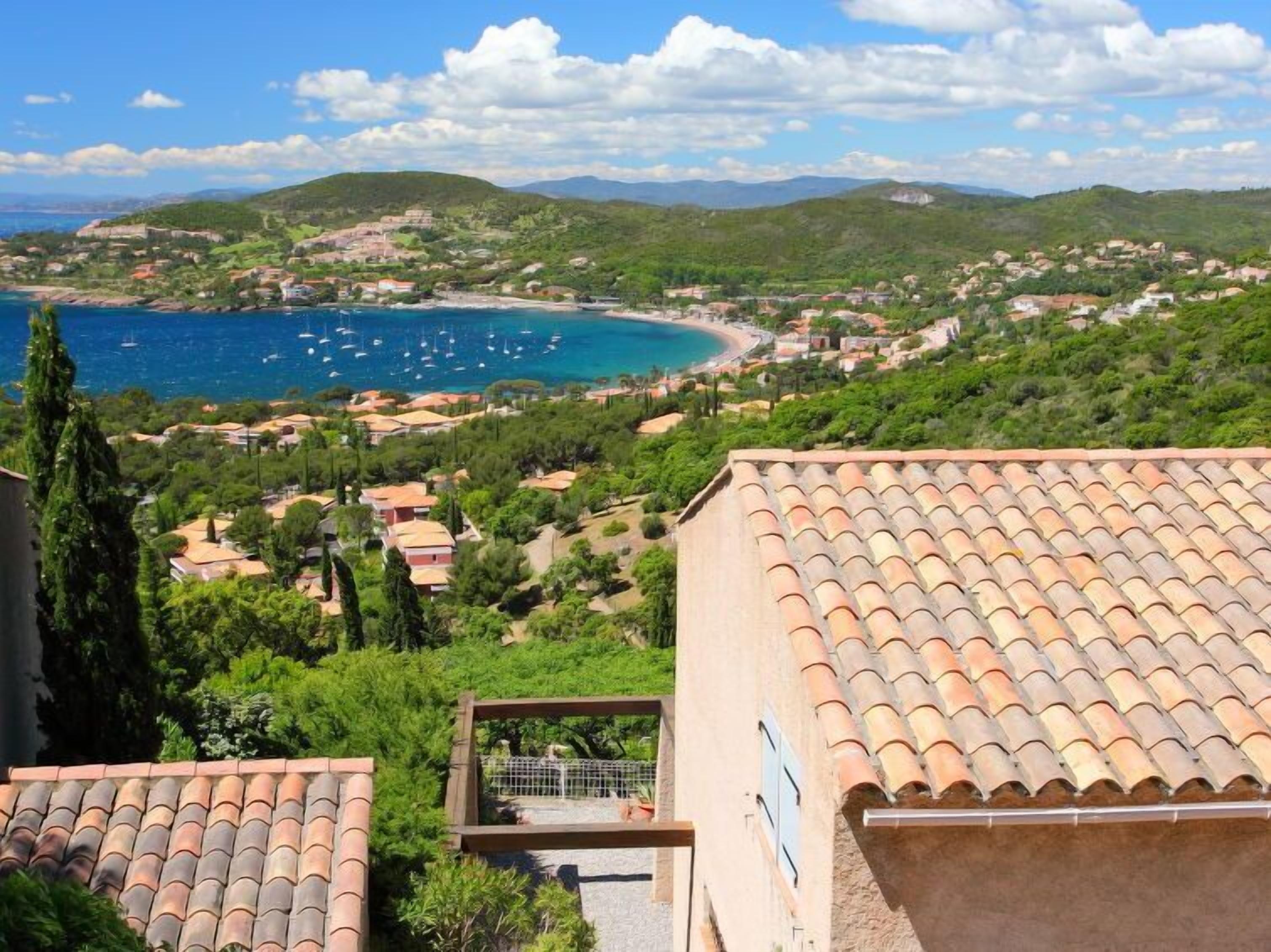 Une ville côtière aux toits recouverts de tuiles en terre cuite, bordée par une mer d’un bleu limpide, et dominée par de luxuriantes collines verdoyantes.