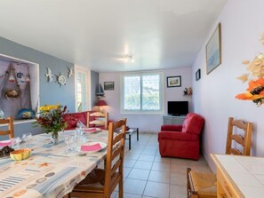 A dining area with a table set for four, a red armchair, and a television in the background.