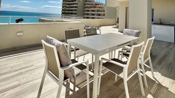 A sunlit outdoor patio with a table and chairs, overlooking a beach and a cityscape. - Luxury Condo Sea View Large Terrace BenalBeach (Benalmádena)
