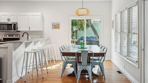 Uma cozinha moderna com armários brancos, uma mesa de jantar de madeira e banquetas.