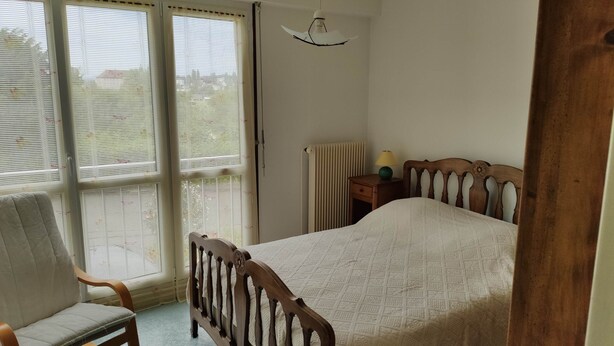 Une chambre à coucher comprenant un lit, une chaise, une table de chevet, une lampe et un radiateur.