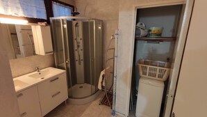 Une salle de bain avec une douche à parois de verre, un lavabo, un miroir et une étagère sur laquelle se trouvent un panier à linge et un récipient.