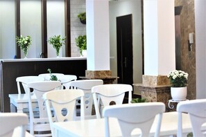 A modern restaurant interior with white chairs and tables, potted plants, and a stone column. - Lucky Star Hotel Da Lat (Da Lat)
