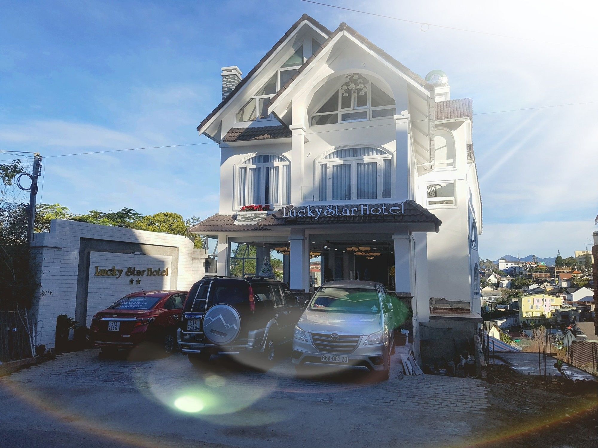 Een gebouw met twee verdiepingen, met een bord waarop 'Lucky Star Hotel' staat. Drie auto's staan ervoor geparkeerd.