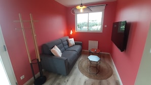 Una habitación con un sofá gris, una mesita, una lámpara de pie y un televisor montado en la pared.