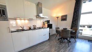 Una cocina moderna con armarios blancos, una campana extractora de acero inoxidable y un comedor con mesa y sillas.
