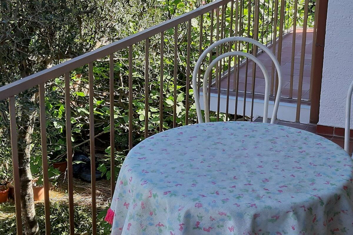 A round table with a floral tablecloth, a white chair, and a metal railing.