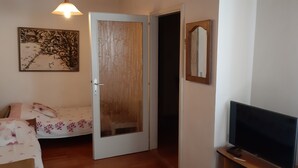 A room with a bed, a television, a door, and a painting on the wall.