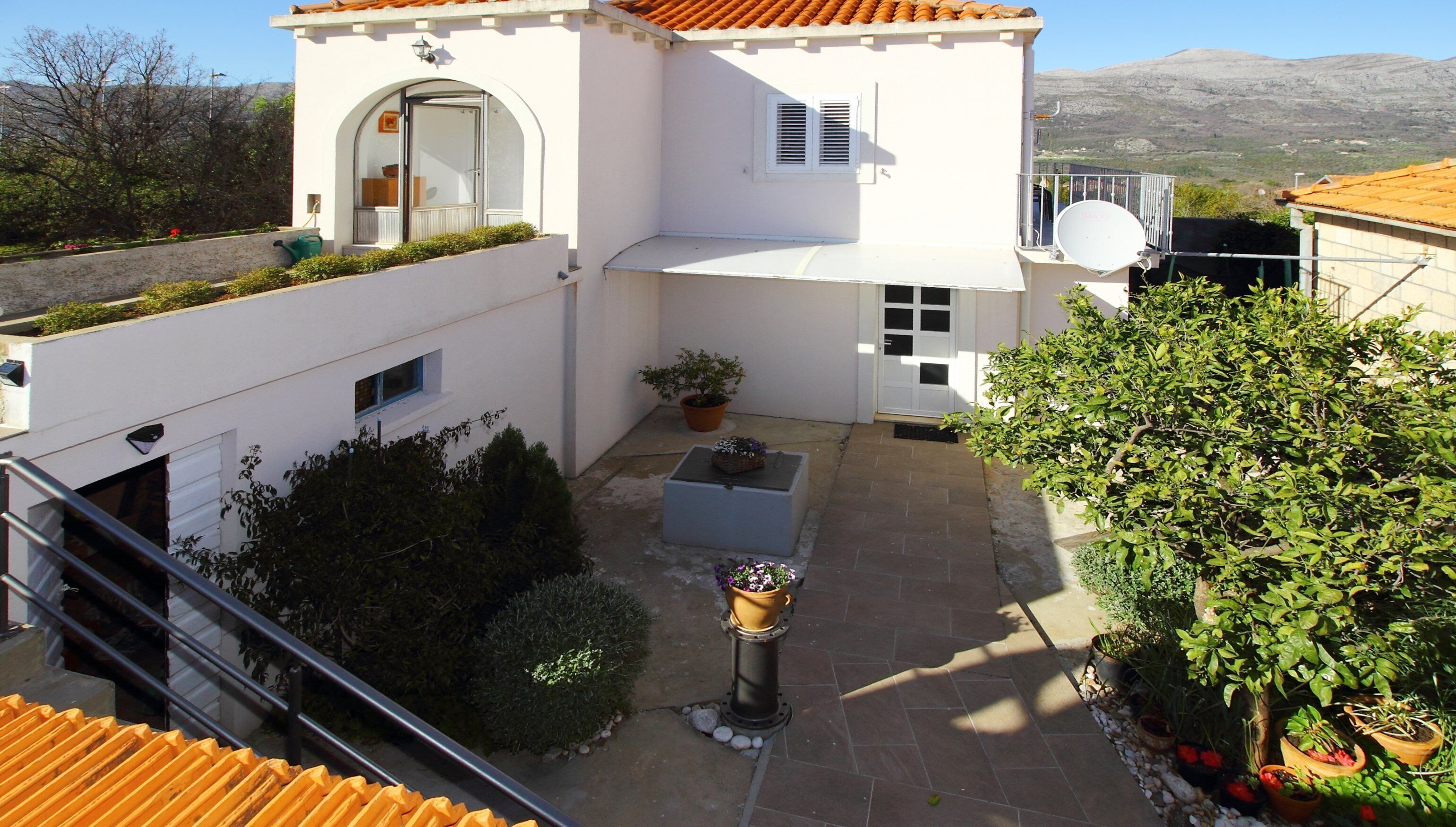 Un bâtiment blanc avec un toit recouvert de tuiles, un petit balcon et un pot de fleurs.