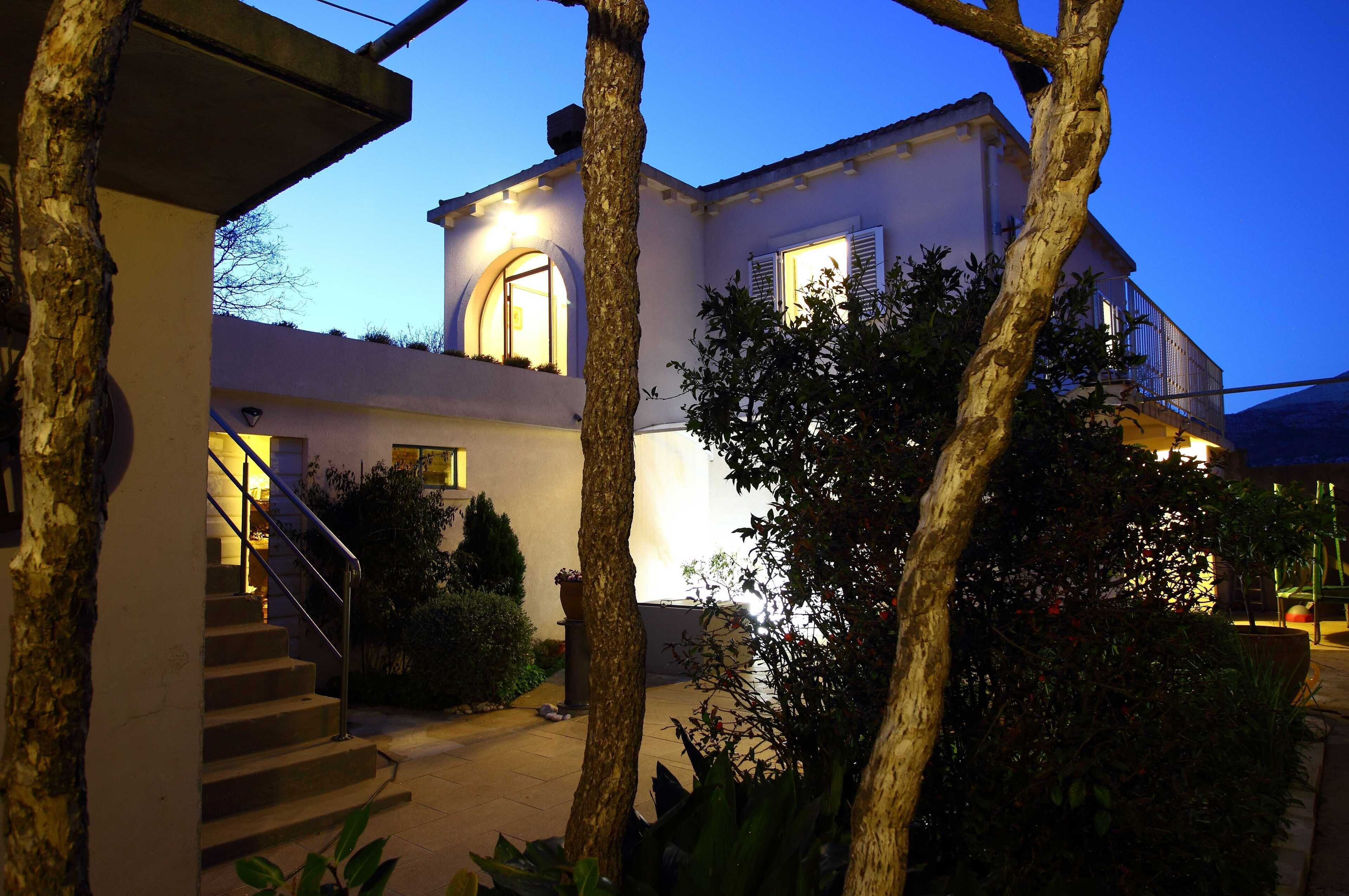 A two-story building with a staircase leading to the entrance, surrounded by trees and plants.