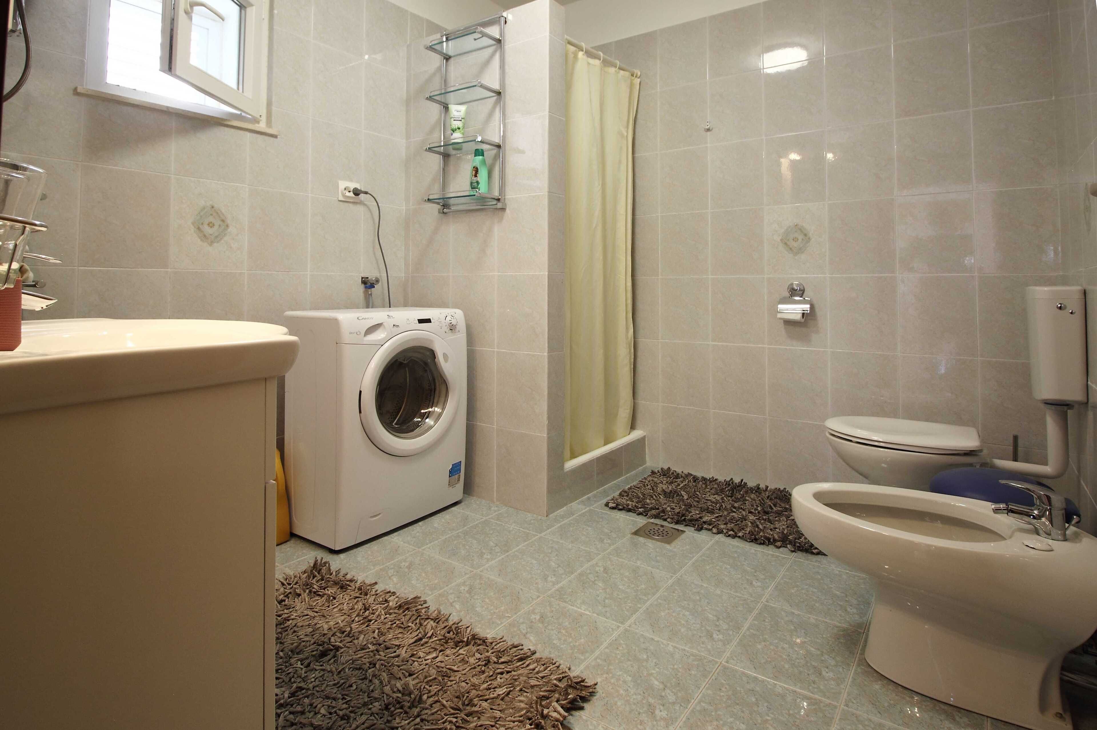 A bathroom with a washing machine, toilet, and a shower area.
