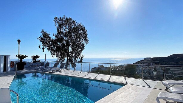 Un ciel d’un bleu éclatant, une piscine avec vue sur la mer et des chaises longues.