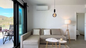 Un salon moderne avec un canapé d’angle, une table basse ronde, un lampadaire et une vue sur l’extérieur.