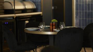 A dining area with a table set for two, a small potted plant, and a grill in the background.