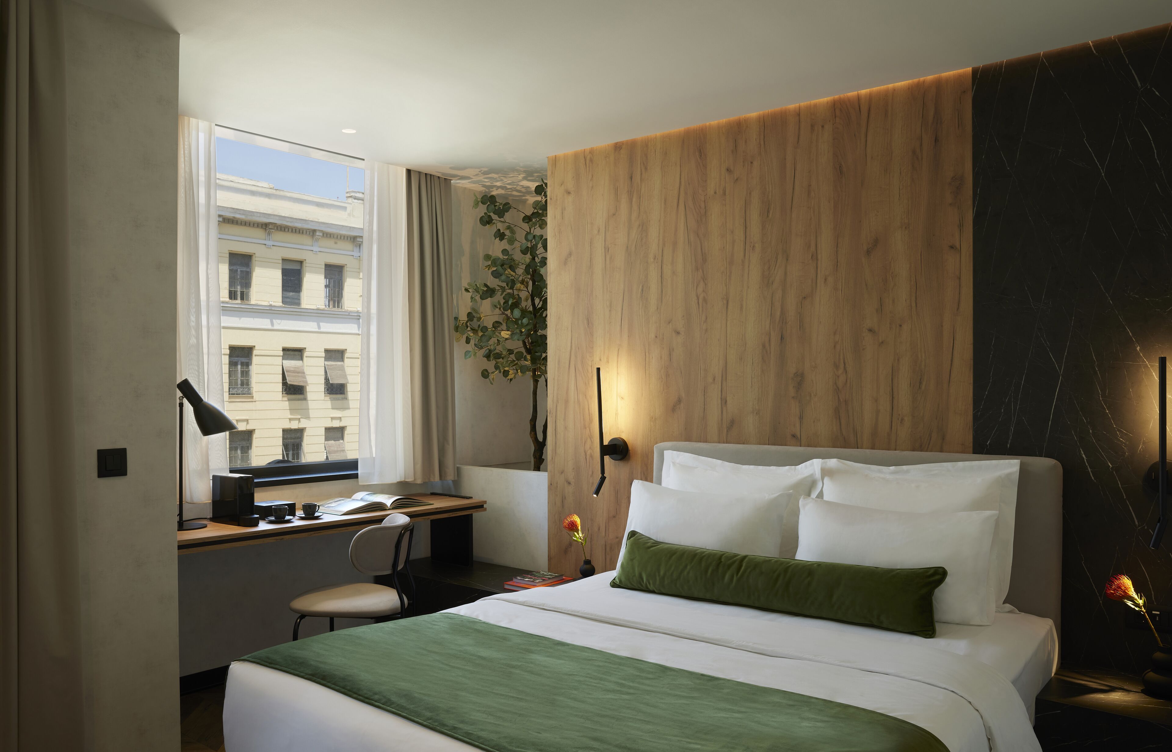 A hotel room with a large bed, a desk, and a window with a view of buildings.