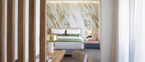 Una habitación de hotel moderna con una pared con diseño de mármol, una cama bien hecha con ropa de cama verde, un escritorio de madera con una silla y una mesita de noche con una lámpara.