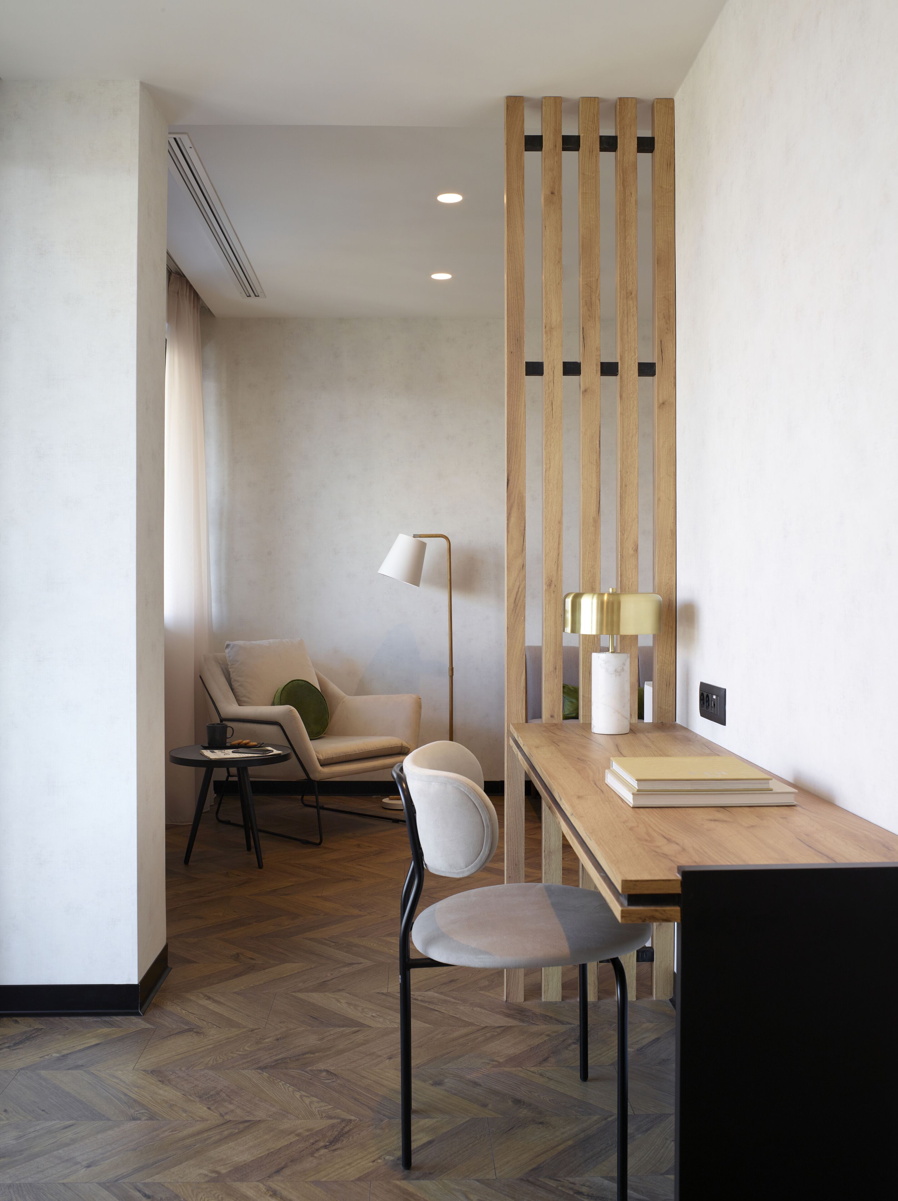 A modern room with a wooden desk, a chair, a floor lamp, and a sofa.