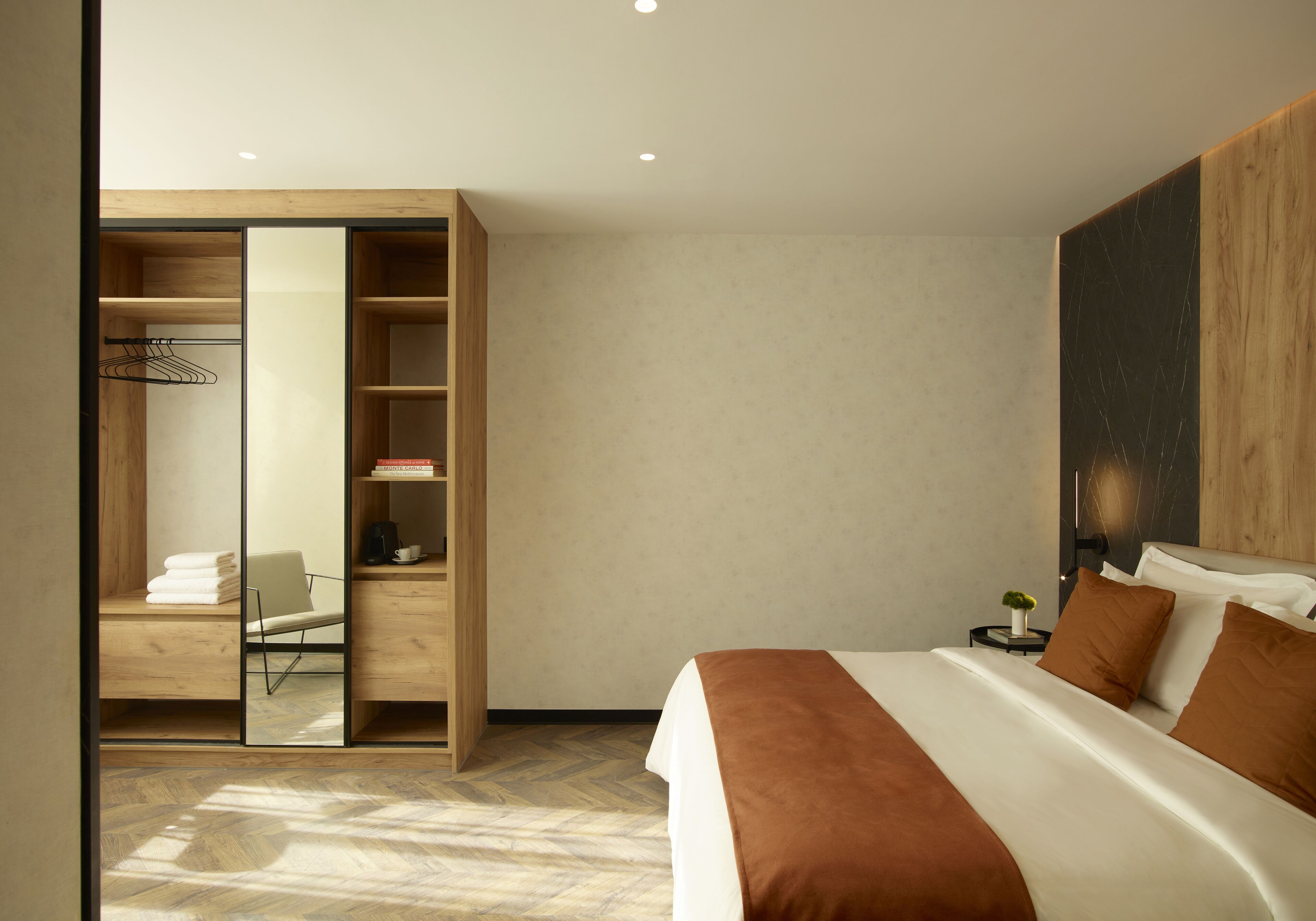 A modern hotel room with a large bed, a wooden wardrobe, and a small bedside table.
