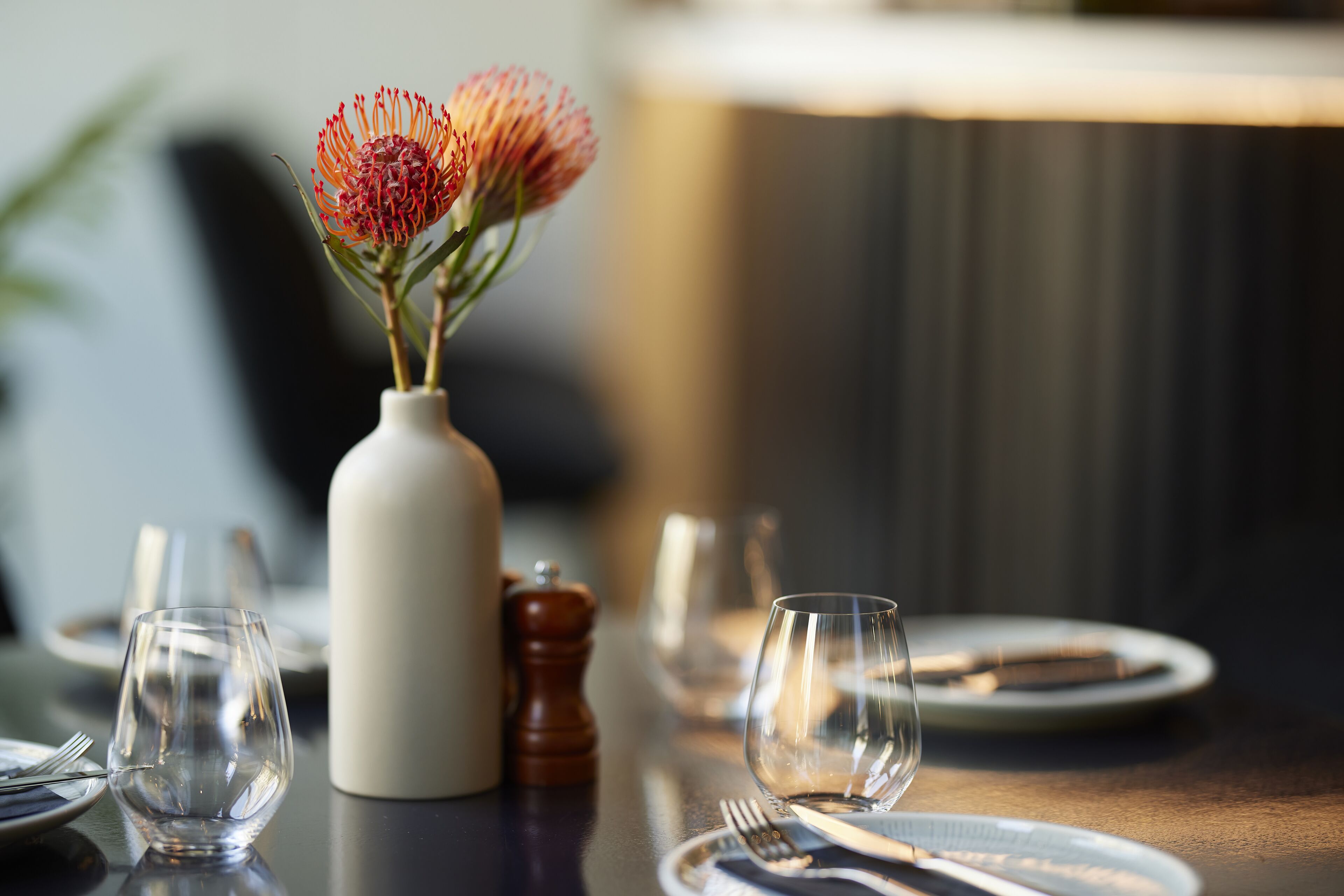 Een eettafel met een bloemenvaas, lege borden en bestek.