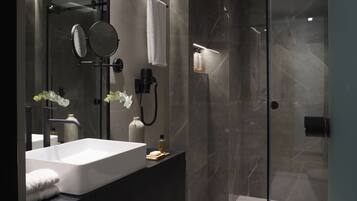 A modern bathroom with a large white bathtub, a glass-enclosed shower, and a vanity with a mirror and a vase of flowers.