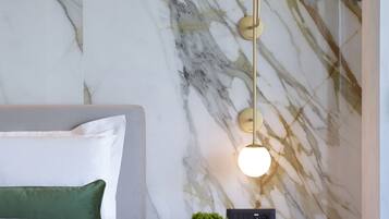Un dormitorio moderno con una pared de mármol, una cama con ropa de cama verde, una mesita de noche con una lámpara y una pequeña planta.